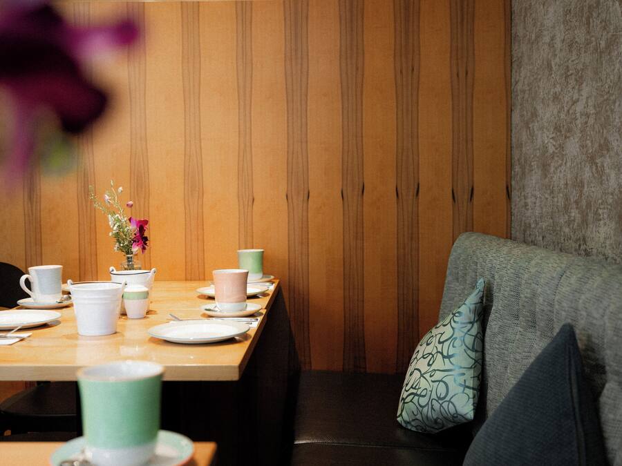 Un comedor con pared de madera, una mesa dispuesta con platos, tazas y un florero con flores.
