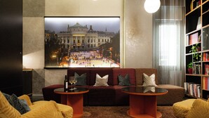A living room with a sofa, two side tables, a bookshelf, and a large framed picture on the wall. - Hotel Capricorno (Vienna)