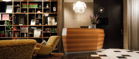 A reception desk with a modern design, a bookshelf filled with books and decorative items, a patterned armchair, and a checkered floor.