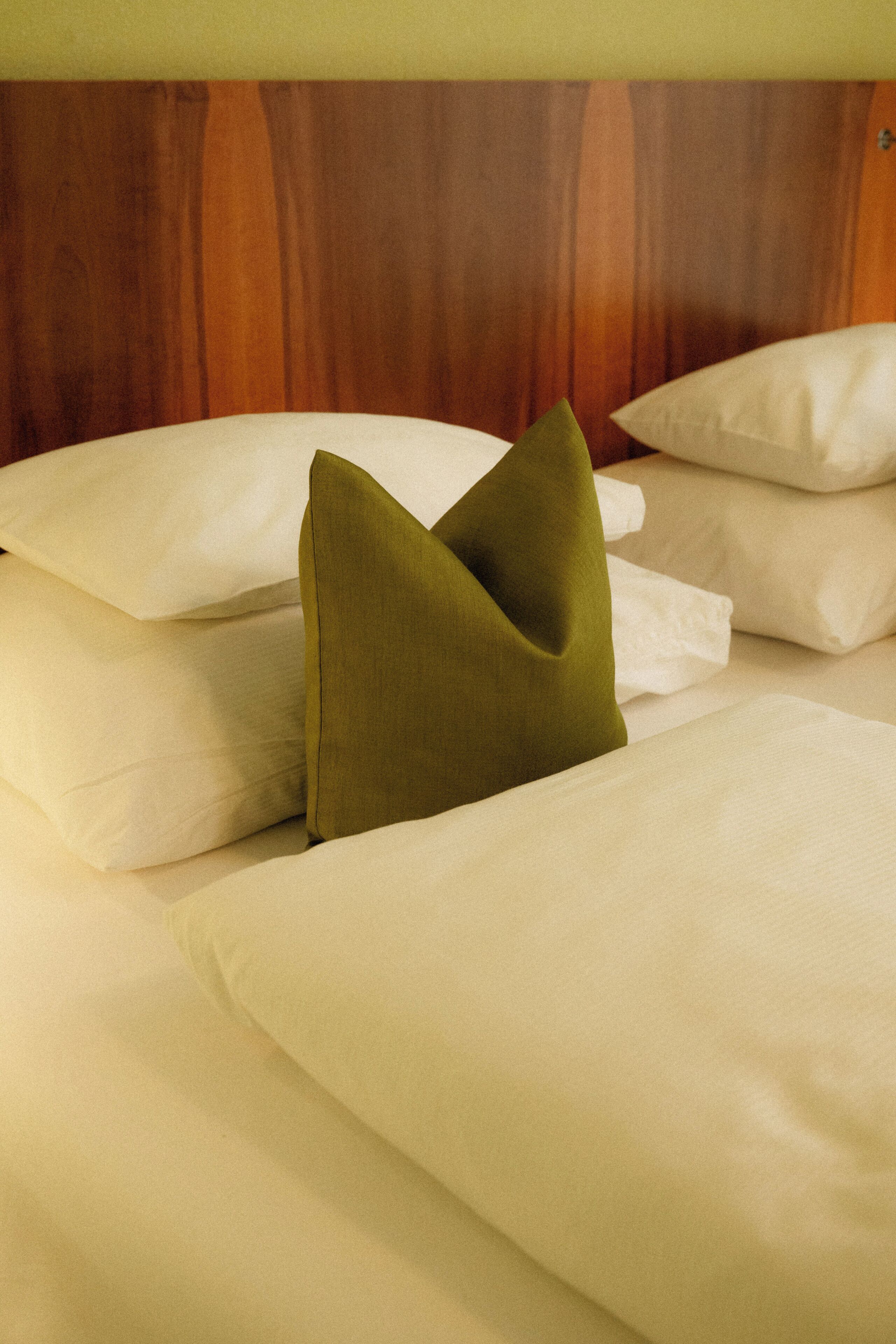 Una cama con sábanas blancas y una almohada verde.