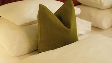 A bed with white linens and a single green pillow.