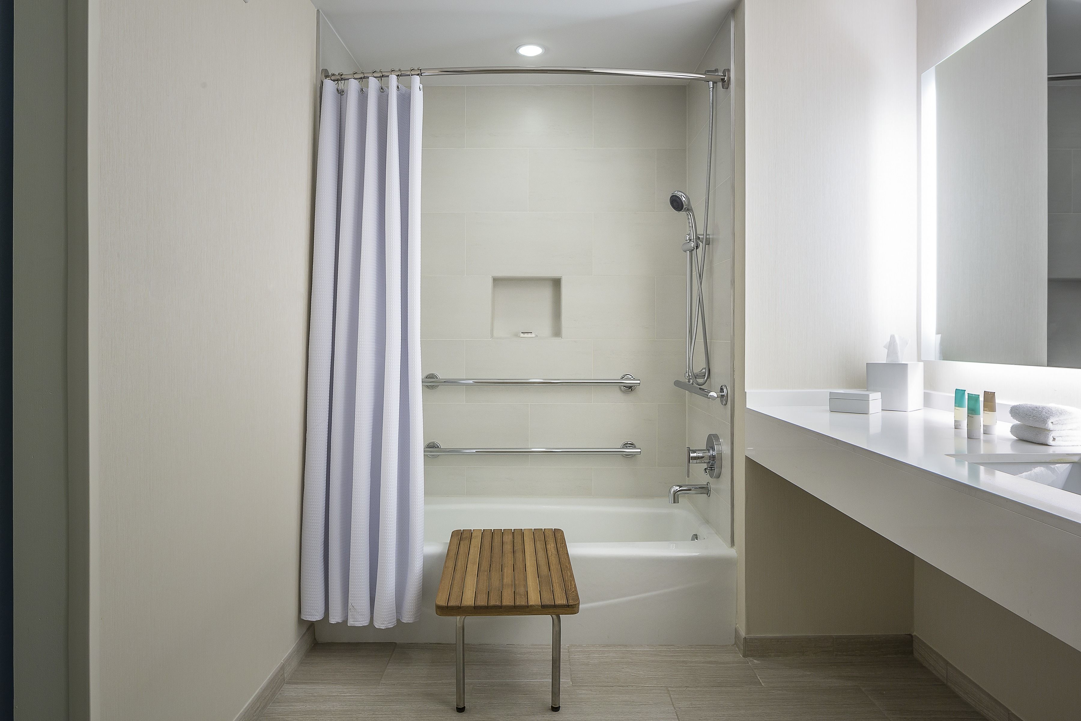 Ein modernes Badezimmer mit Dusche, einem kleinen Holzschemel, einer Badewanne und einem Waschtisch mit Spiegel.