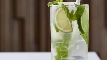 A tall glass with a straw, filled with ice cubes, lime slices, and mint leaves.