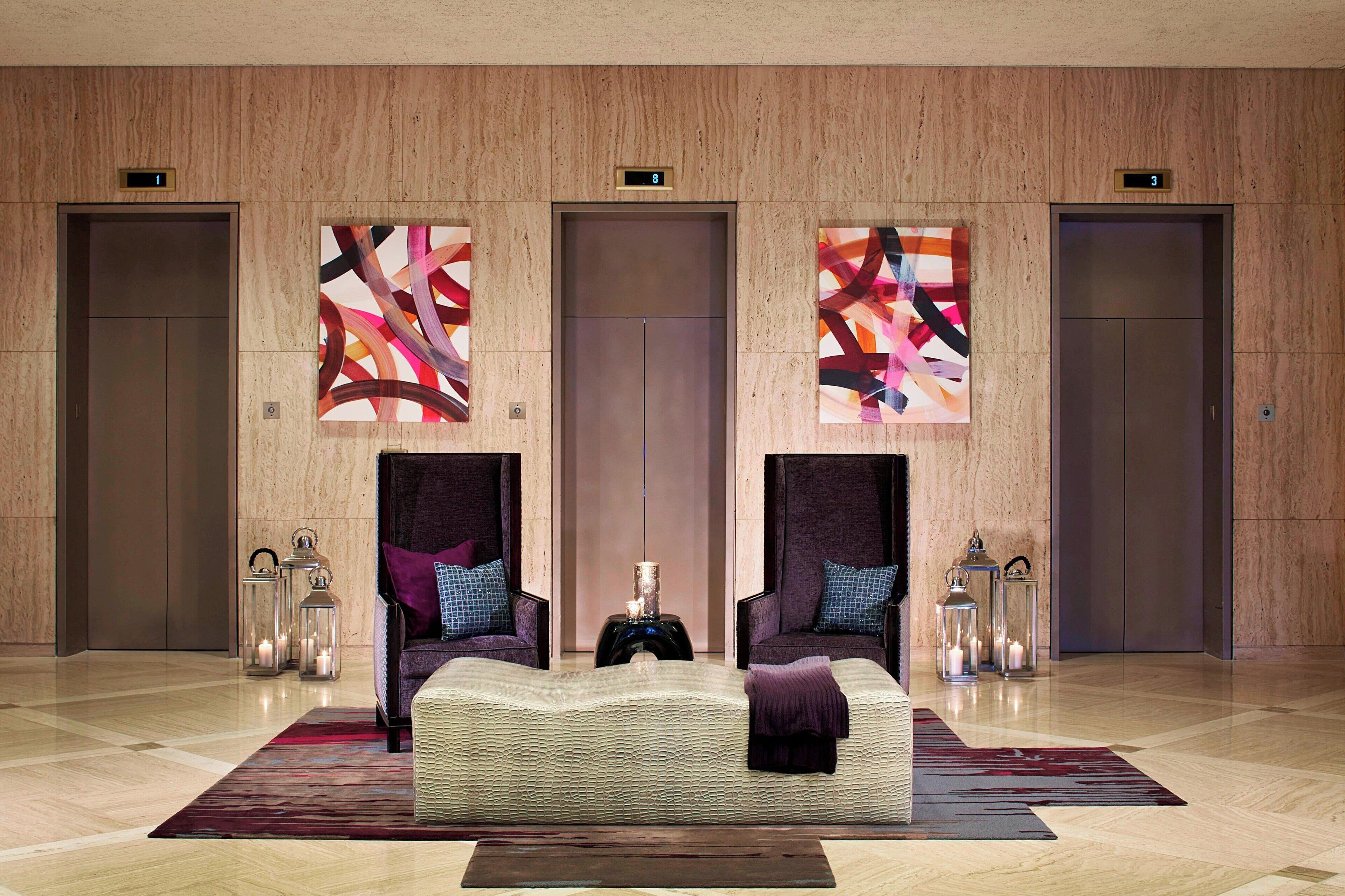 A lobby with a large bed, two armchairs, and three wall-mounted artworks.