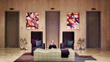 A lobby with a large bed, two armchairs, and three wall-mounted artworks.