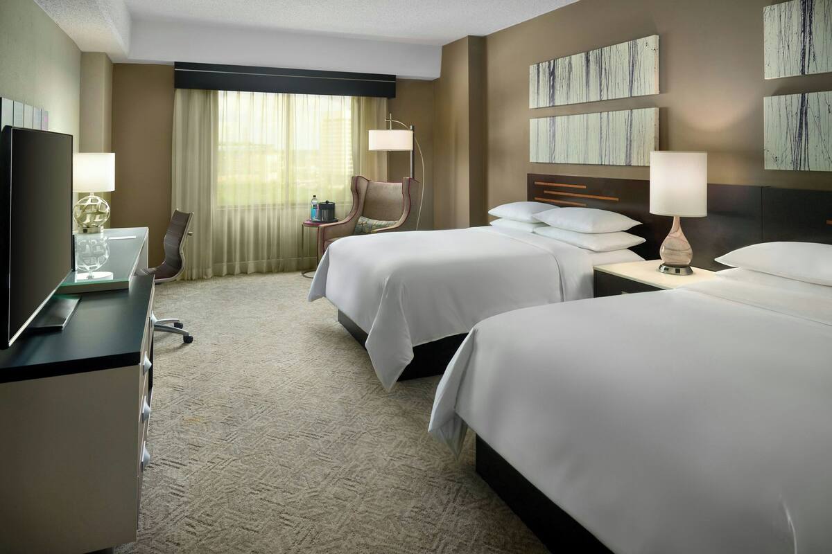 A hotel room with two beds, a desk with a computer, a chair, and a TV.
