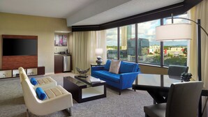 A hotel room with a large window, a flat-screen TV, a blue sofa, a white armchair, and a small table. - Renaissance Atlanta Waverly Hotel & Convention Center (Atlanta)