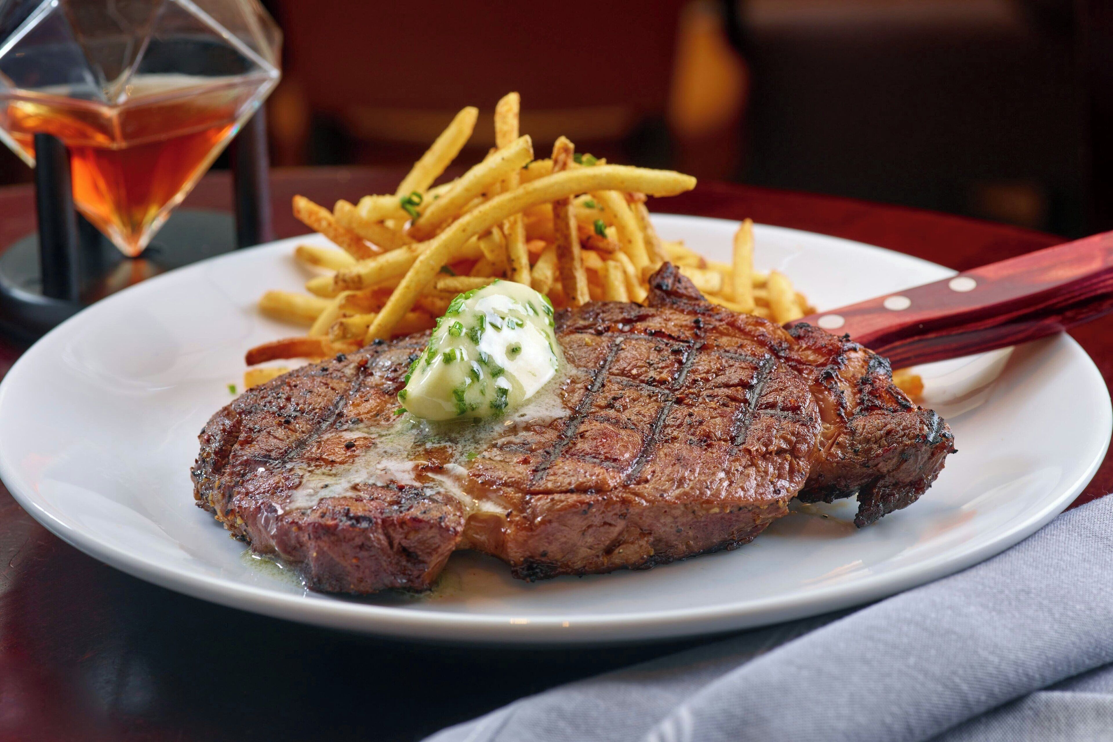 A steak with a pat of butter on a plate, accompanied by French fries.