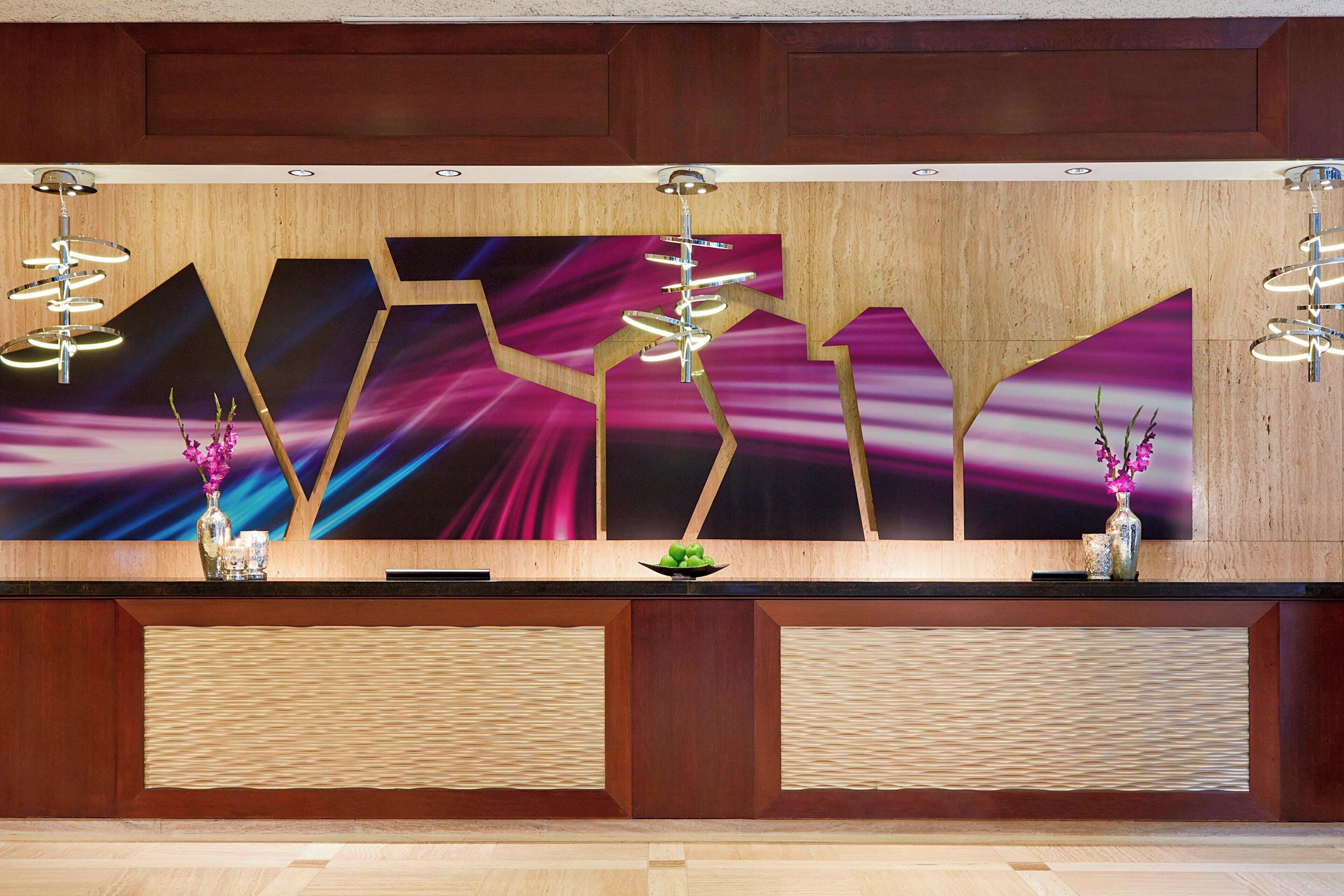 A reception desk with a modern design, featuring a large abstract painting, two decorative vases, and a unique light fixture.
