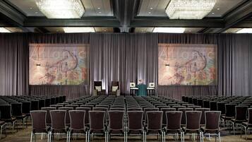 A conference room with rows of chairs, a large screen displaying 'Atlantis', and a chandelier.