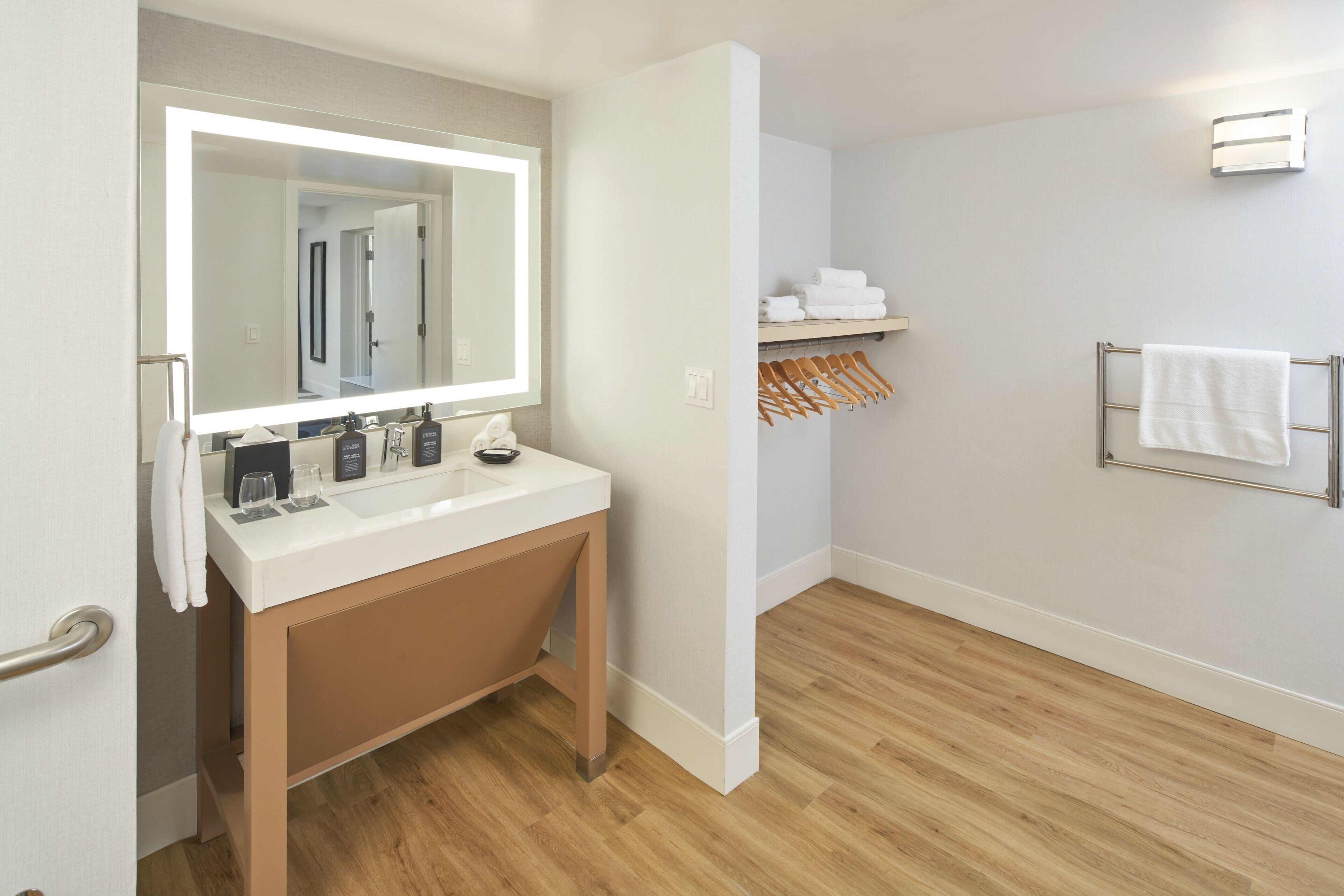 A modern bathroom with a large mirror, white sink, wooden vanity, and a towel rack.