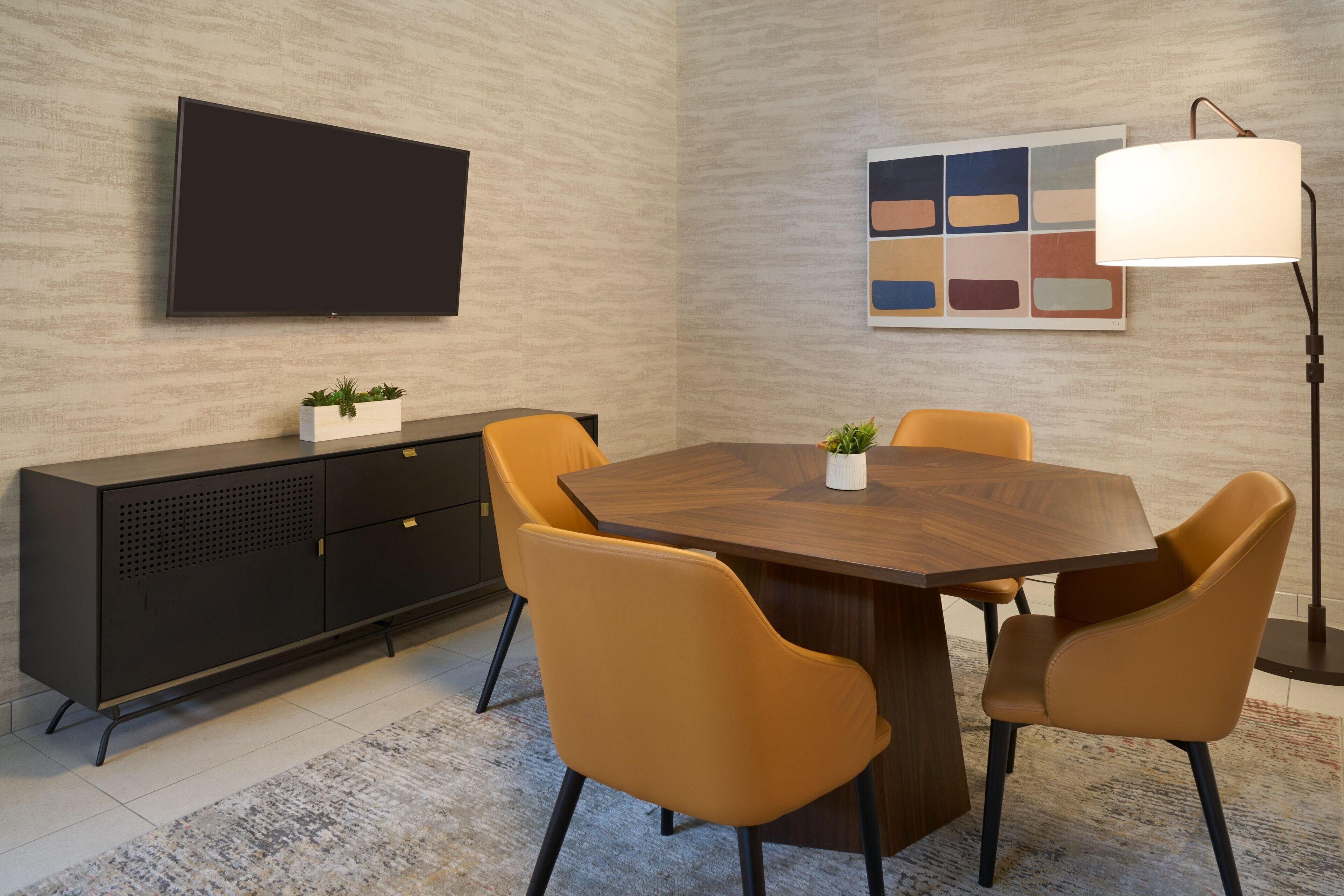 Un espace repas moderne avec une table en bois, deux chaises jaunes, un meuble noir, un téléviseur à écran plat et un lampadaire.