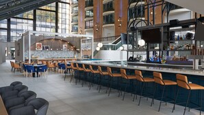 Zona de bar moderna con techos altos, una barra larga con taburetes y vistas al exterior a través de amplias ventanas.