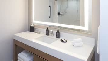 A modern bathroom with a large mirror, a double sink, and a vanity with a towel rack.