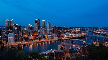Un horizonte urbano al anochecer con edificios iluminados, un río y un puente.