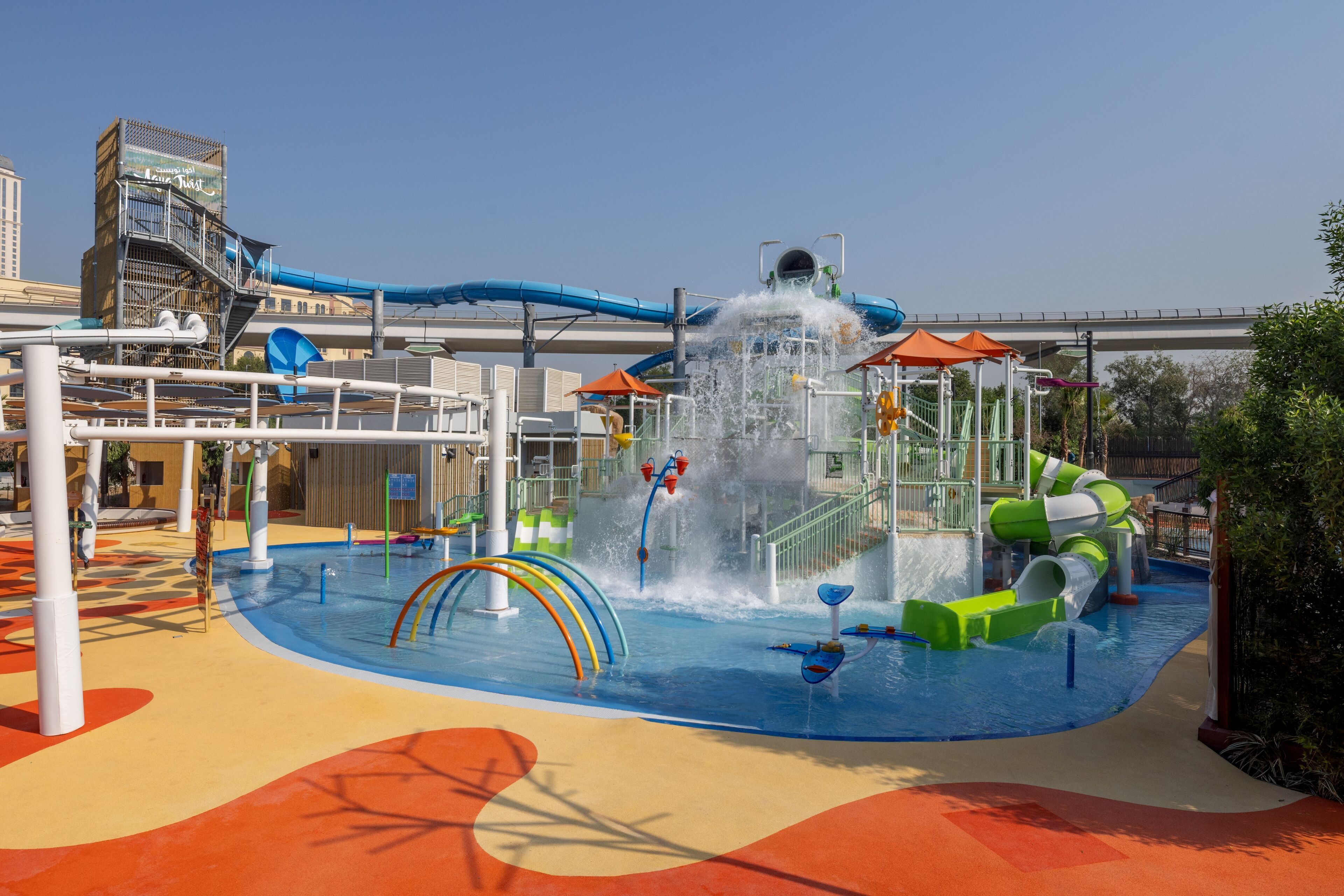 Parque acuático con un tobogán de agua grande, varias estructuras de juego y una zona de juegos con agua.