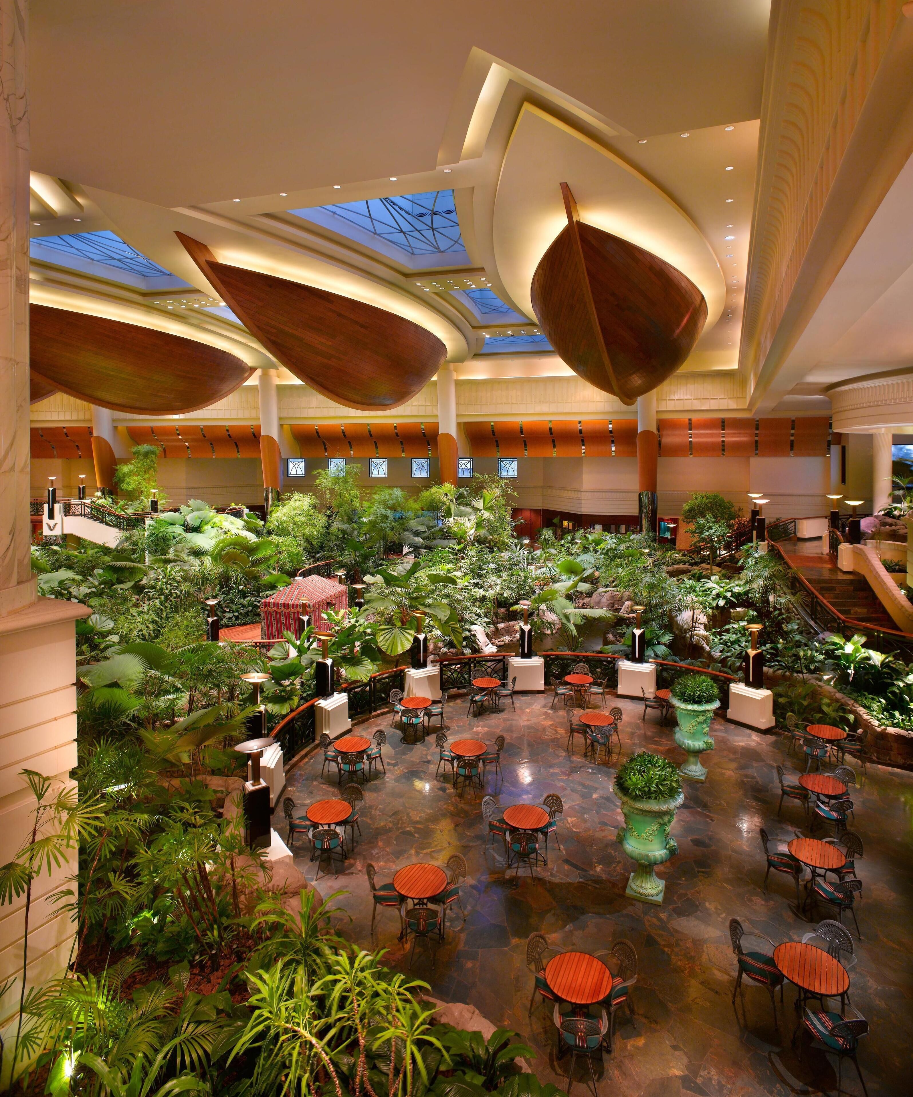 A spacious indoor atrium with a central garden area, multiple seating arrangements, and a high ceiling with natural light.