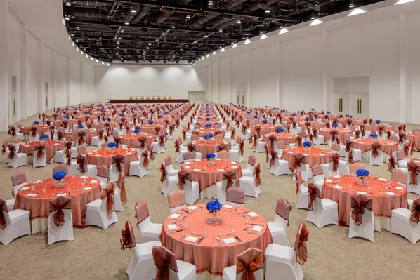 Un amplio salón de conferencias con varias mesas redondas, cada una con sillas blancas y manteles naranjas.