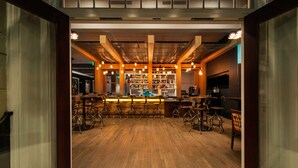 A bar area with wooden flooring, bar stools, and hanging lights.