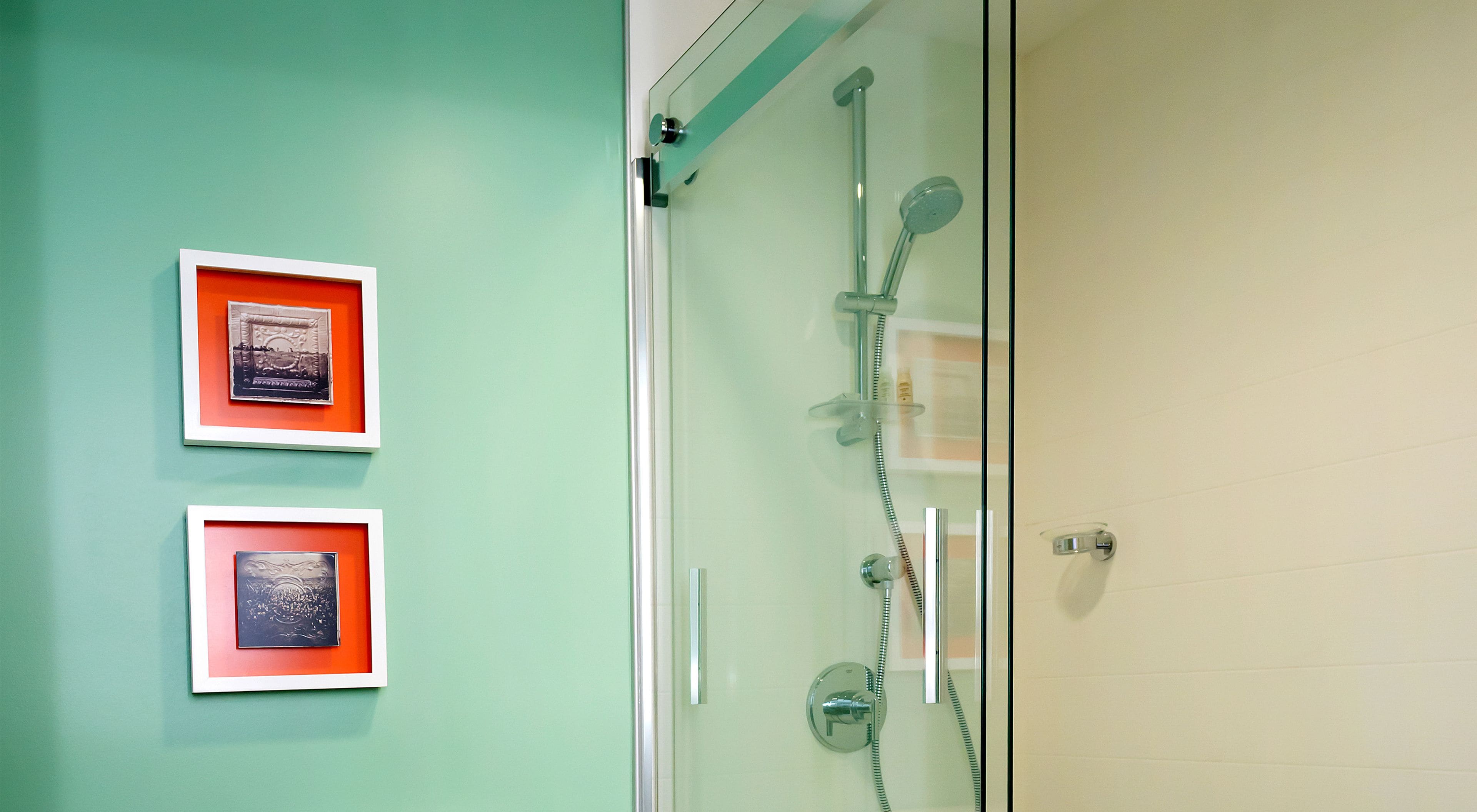 A bathroom with a glass shower enclosure, two framed pictures on the wall, and a plain tiled wall.