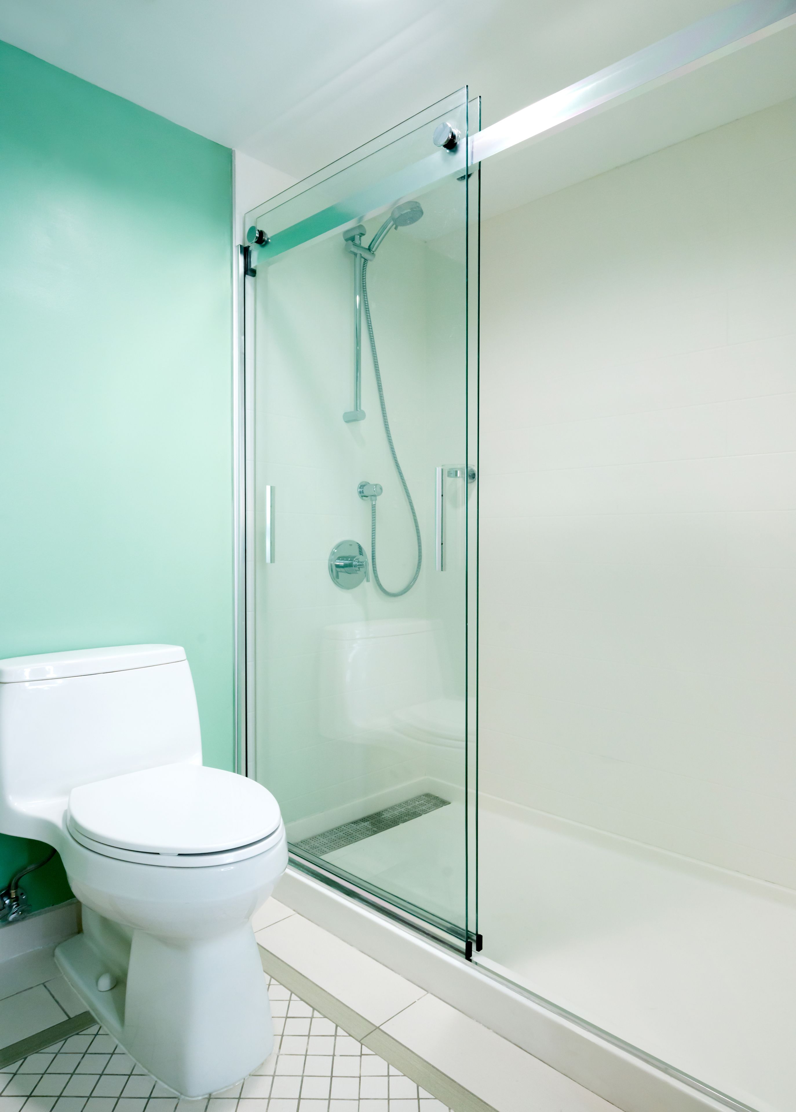 Un baño moderno con ducha de vidrio, inodoro blanco y pared verde.