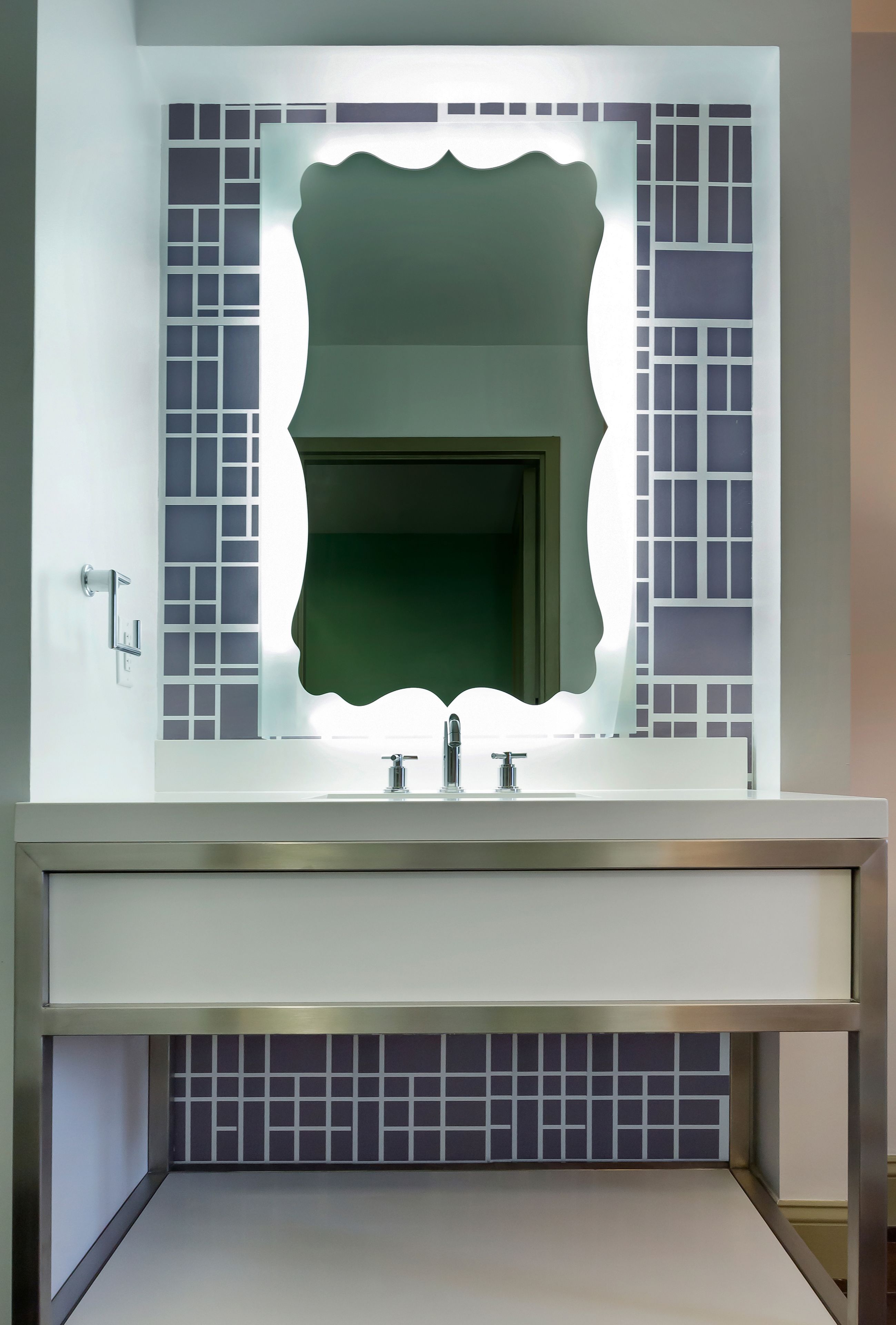 A bathroom with a modern vanity, a mirror with a geometric frame, and a tiled backsplash.