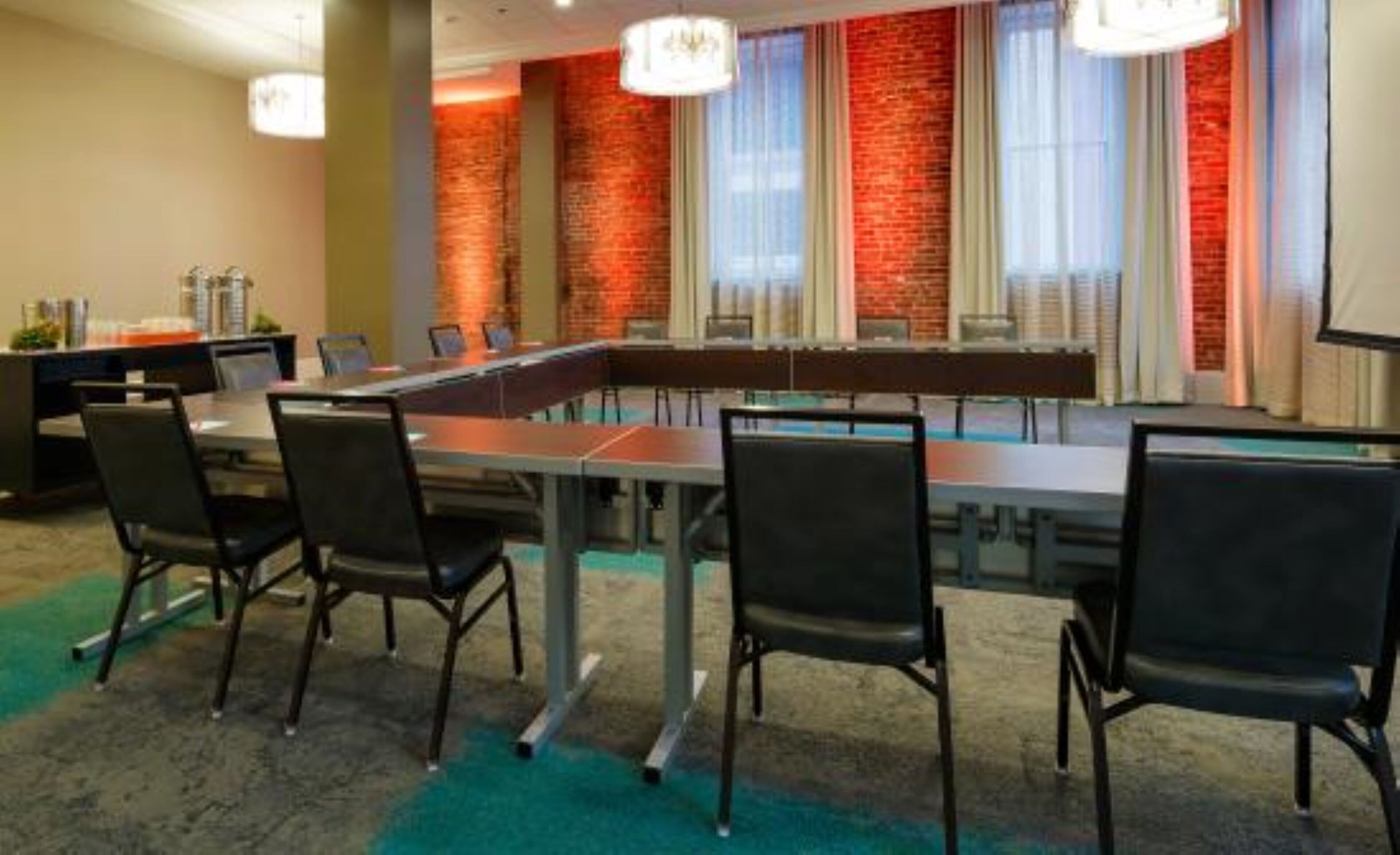 A conference room with a long table, black chairs, and a brick wall with windows.