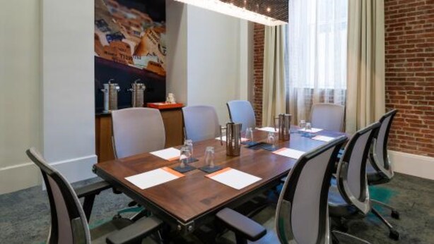 Een vergaderzaal met een lange tafel, zes stoelen en een bakstenen muur.