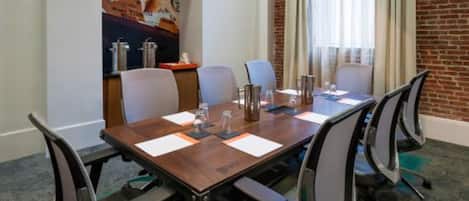 A conference room with a long table, six chairs, and a brick wall.