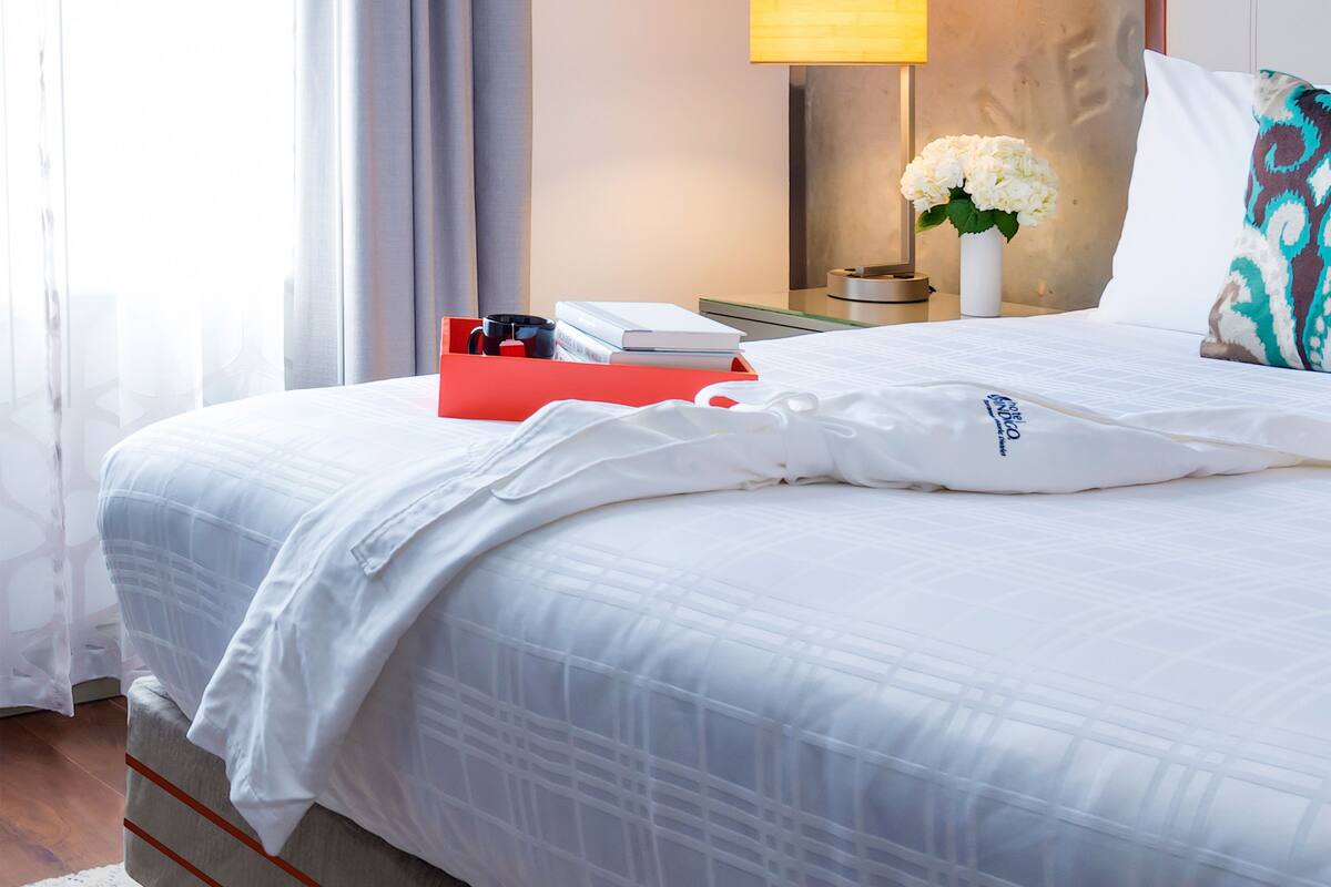 A neatly made bed with a white comforter, a red box, and a white pillow with a logo.