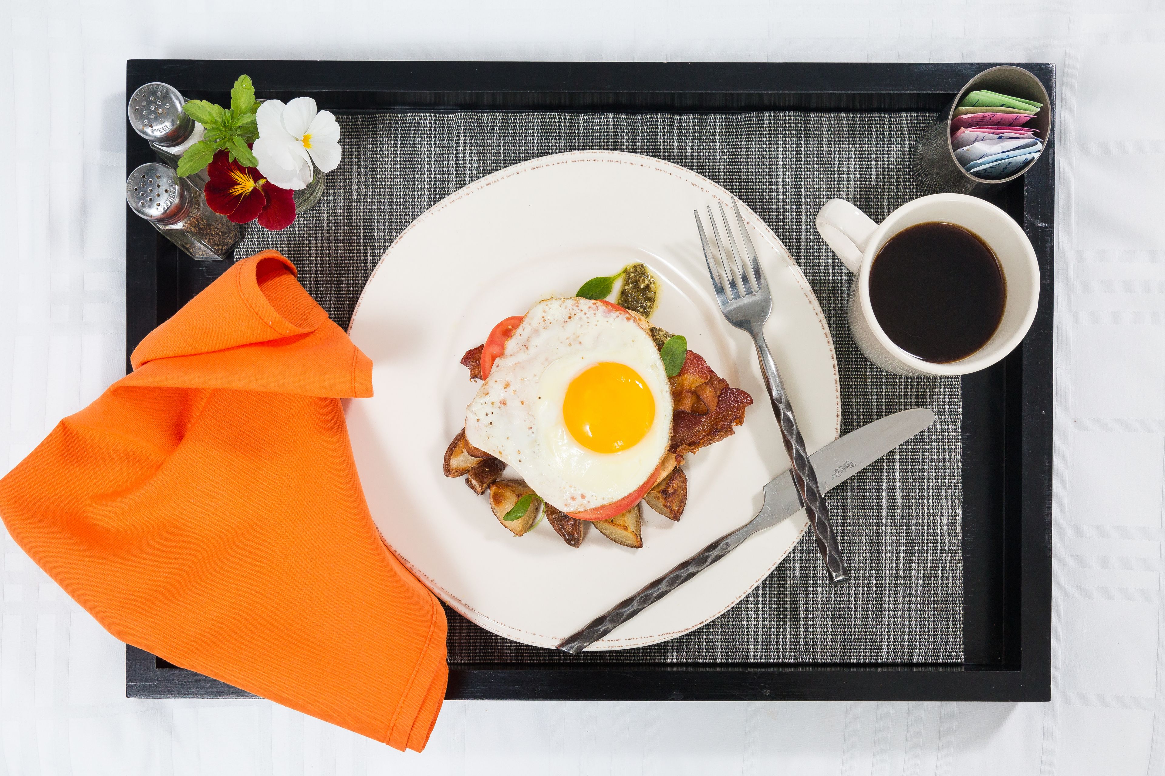 A tray with breakfast items including eggs, bacon, and potatoes, a cup of coffee, and a napkin.
