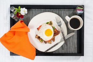 A tray with breakfast items including eggs, bacon, and potatoes, a cup of coffee, and a napkin.
