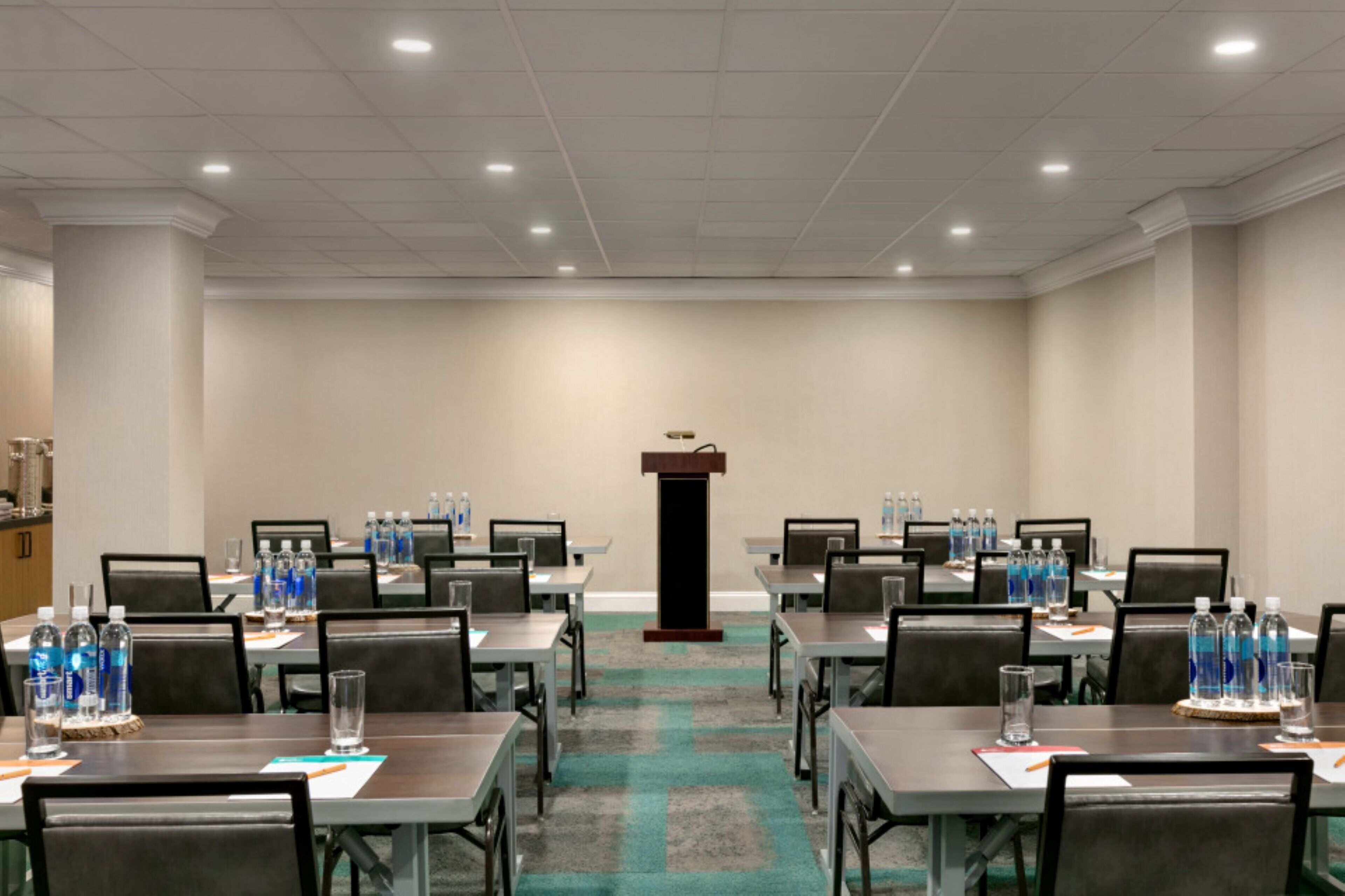 A conference room with tables, chairs, water bottles, and a podium.