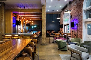 Zona de bar moderna con mesas de madera, taburetes y lámparas colgantes.