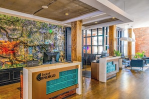 Un vestíbulo de hotel con una recepción, un mural grande en la pared y una zona de estar con vista a una pared de ladrillo.