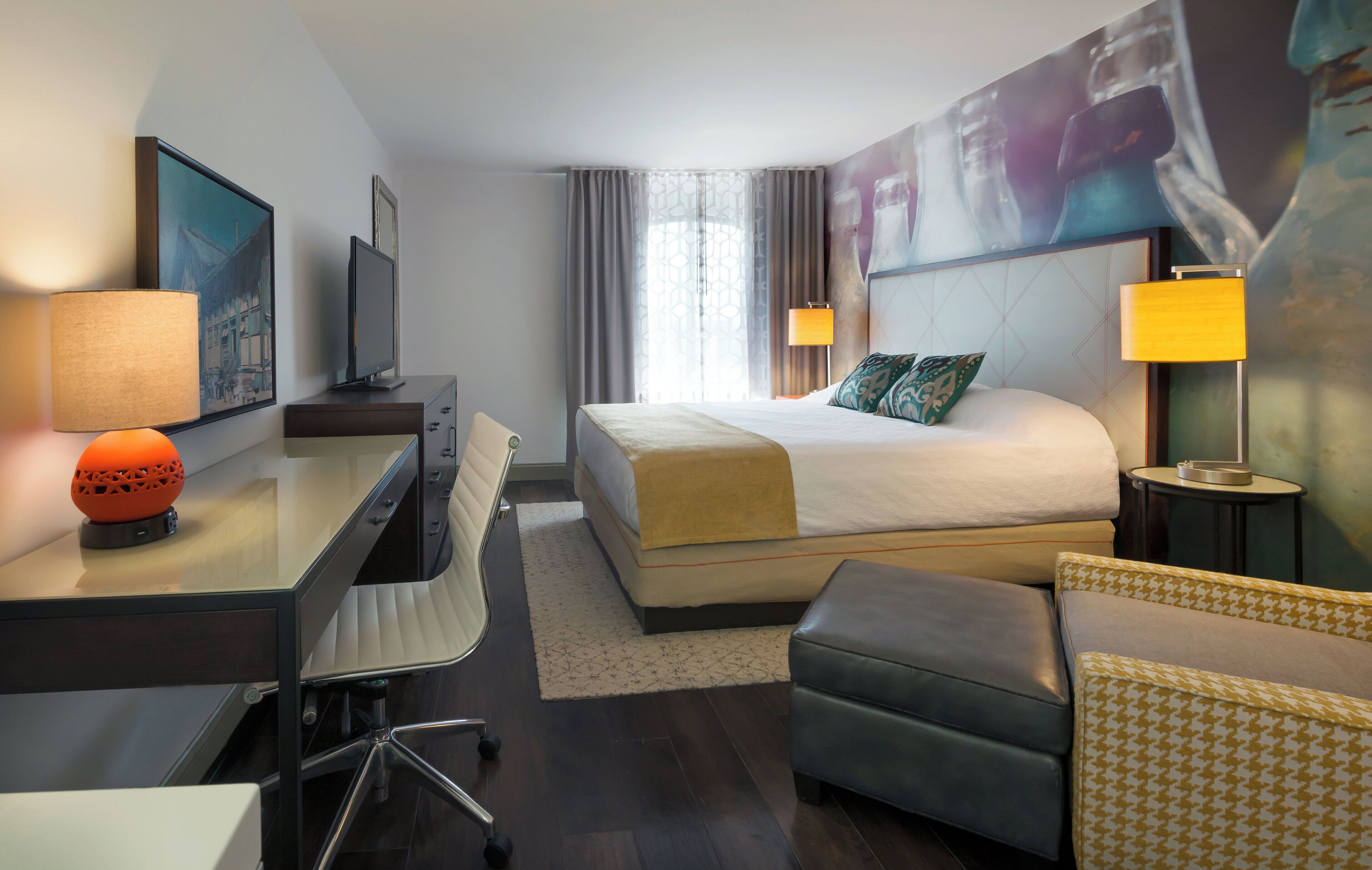 Ein Hotelzimmer mit Bett, Schreibtisch, Stuhl und einem kleinen Tisch mit Lampe.