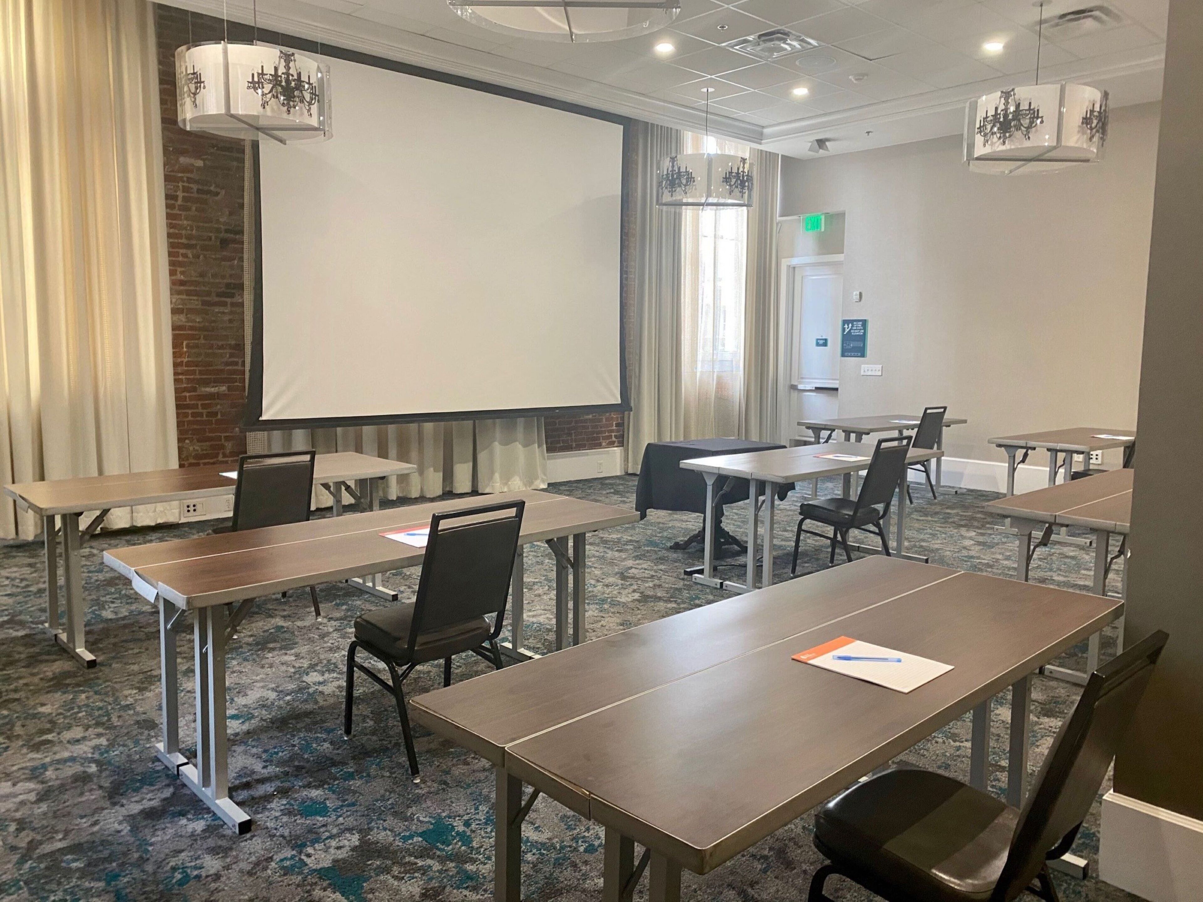 Un salón de conferencias con mesas, sillas, una pantalla de proyector y candelabros.