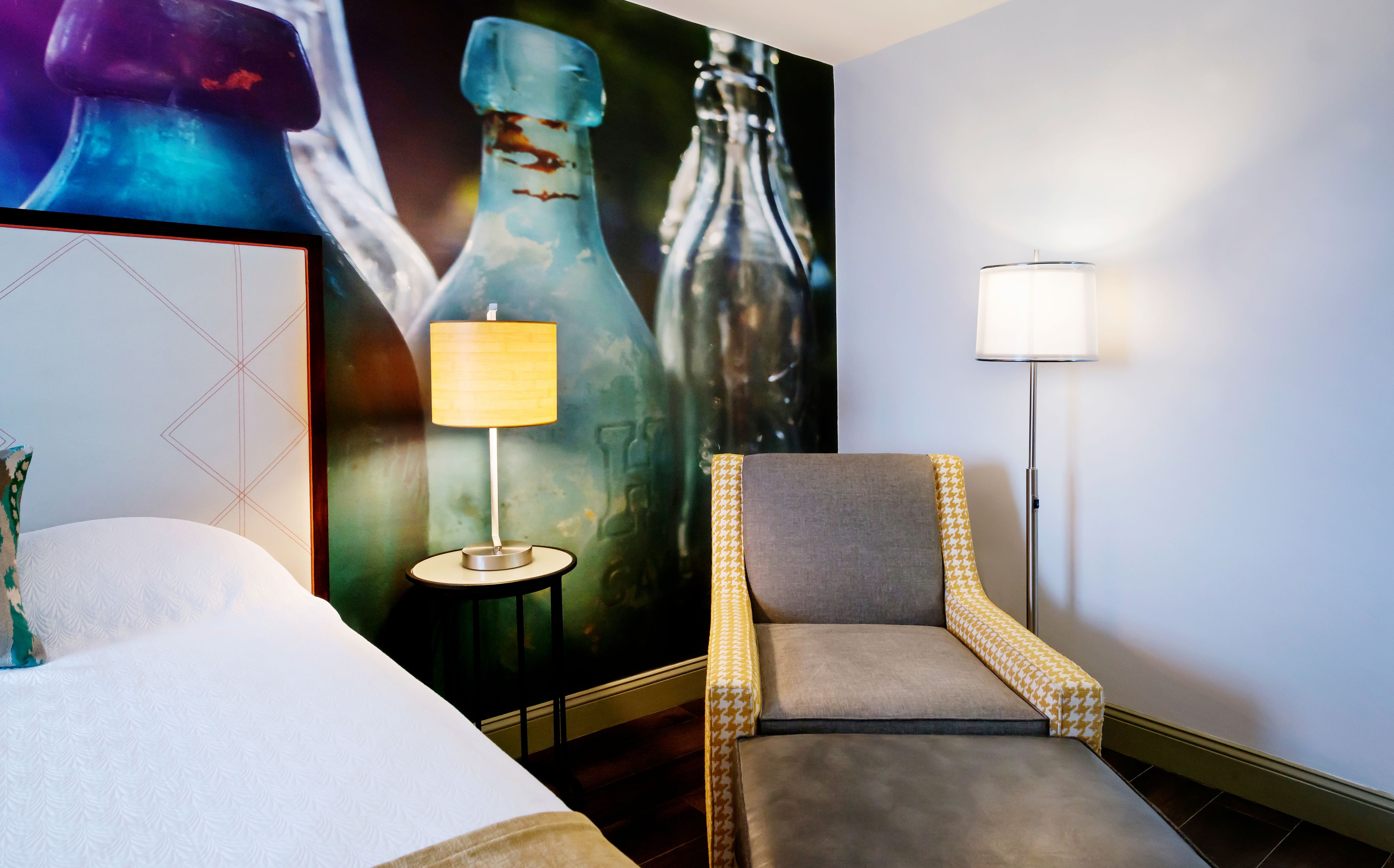 Habitación de hotel con cama, una silla, una lámpara y un cartel grande en la pared.