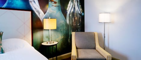Habitación de hotel con cama, una silla, una lámpara y un cartel grande en la pared.