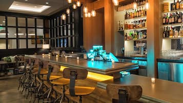 A bar area with a long counter, bar stools, and shelves stocked with liquor bottles.