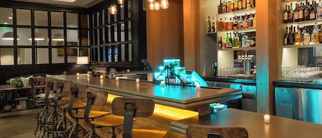 Una zona de bar con una barra larga, taburetes y estantes llenos de botellas de licor.