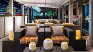 A modern outdoor seating area with wicker furniture and patterned cushions, featuring a view of the cityscape at night.