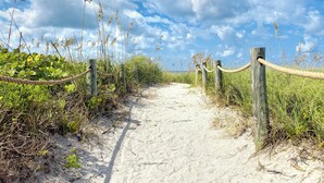 A sandy path with wooden posts and rope barriers, surrounded by grass and plants.