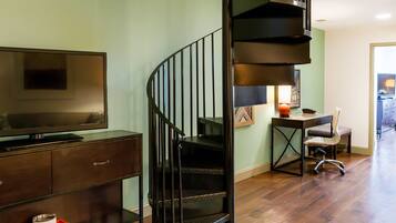 A modern living room with a flat-screen TV, a wooden cabinet, a desk with a chair, and a spiral staircase.