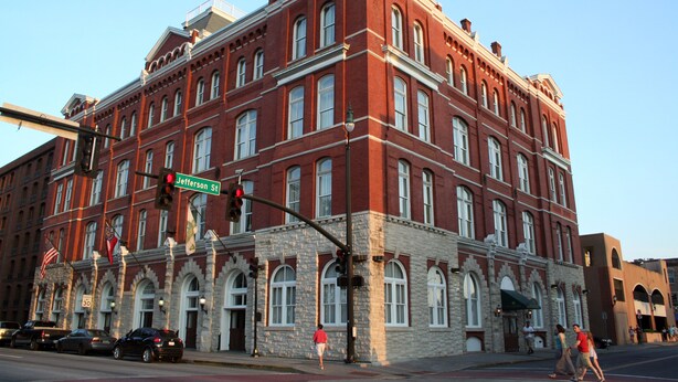 A historic red brick building with multiple windows and a flag on top.