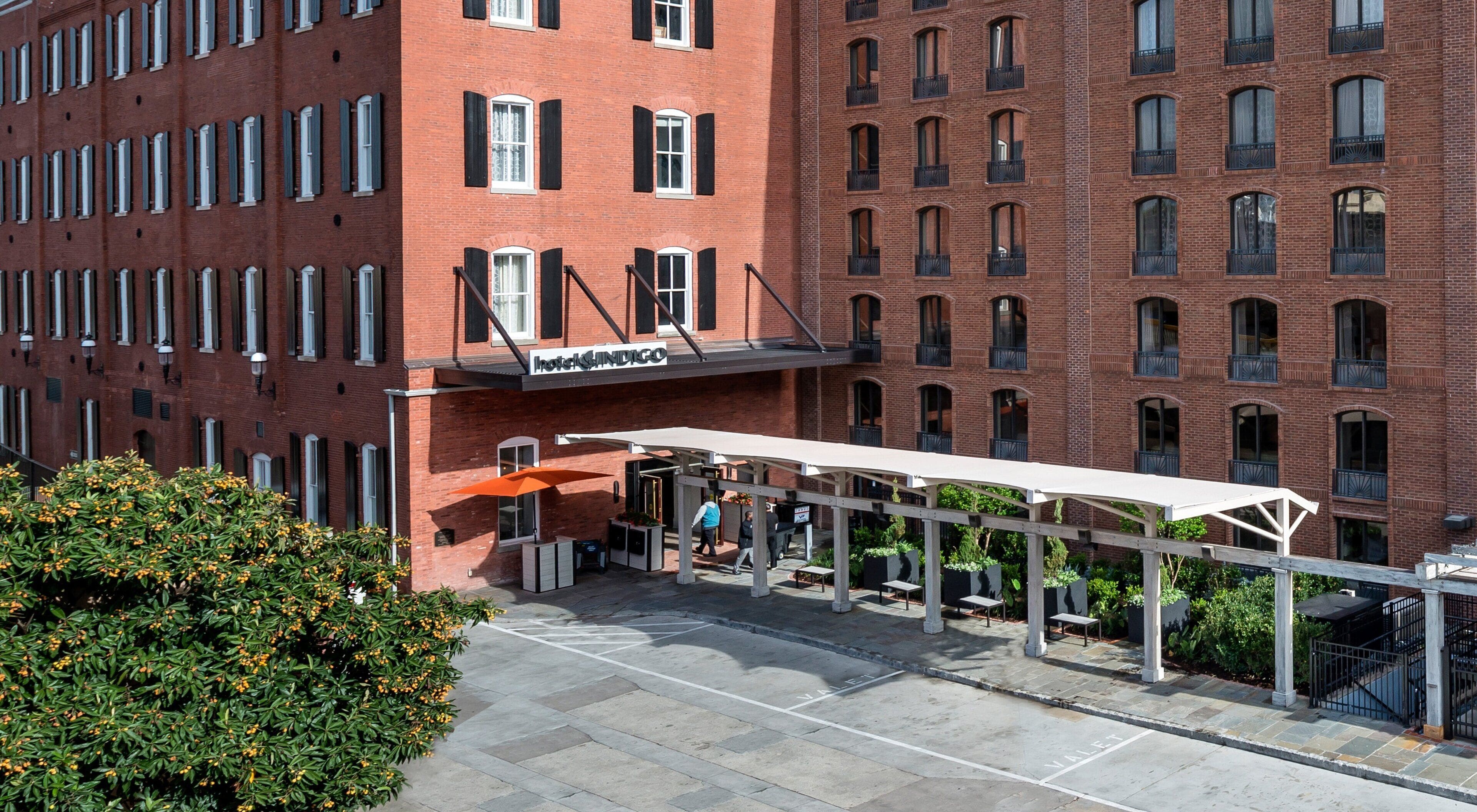 Ein Hotel mit roter Backsteinfassade, zahlreichen Fenstern und einer überdachten Außenbereicherung mit Sitzgelegenheiten.