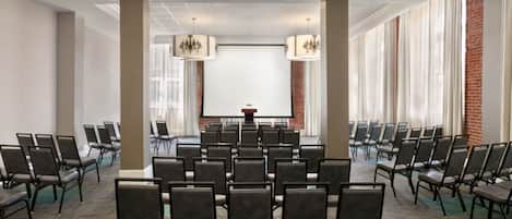 Un salón de conferencias con filas de sillas, una pantalla de proyector y candelabros.