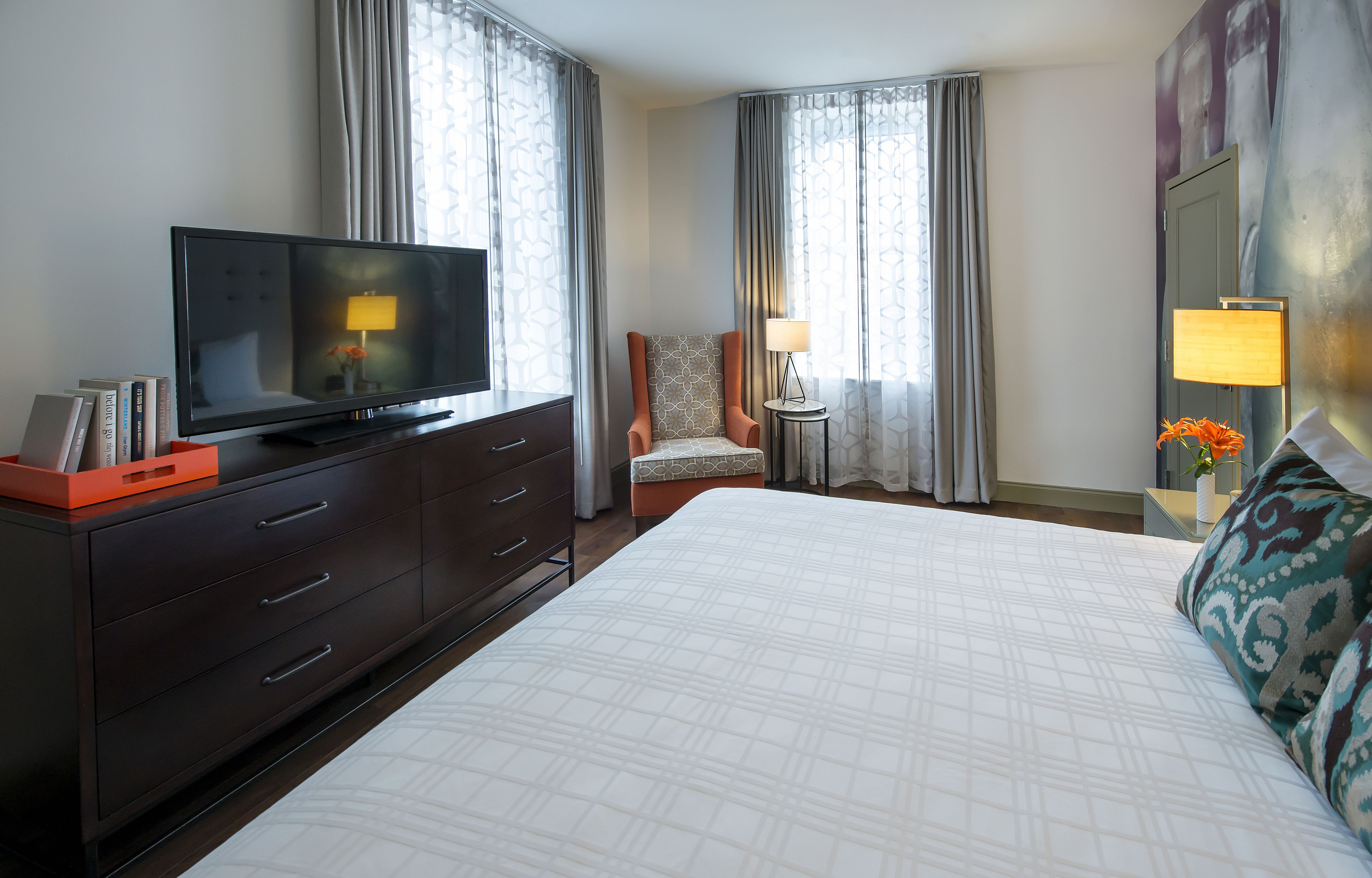 Una habitació d'hotel amb un llit gran, un televisor sobre una petita taula, una cadira i dues làmpades.
