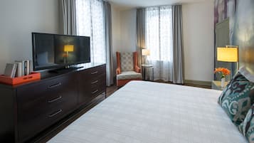 Una habitació d'hotel amb un llit gran, un televisor sobre una petita taula, una cadira i dues làmpades.