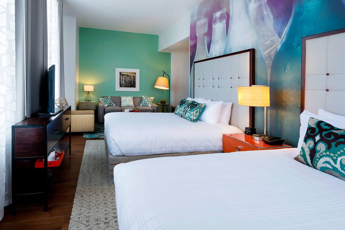 A hotel room with two beds, a desk, a chair, a TV, and a painting on the wall.